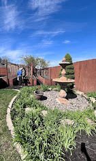 Backyard garden with a tiered stone fountain, rock bed, and border plants