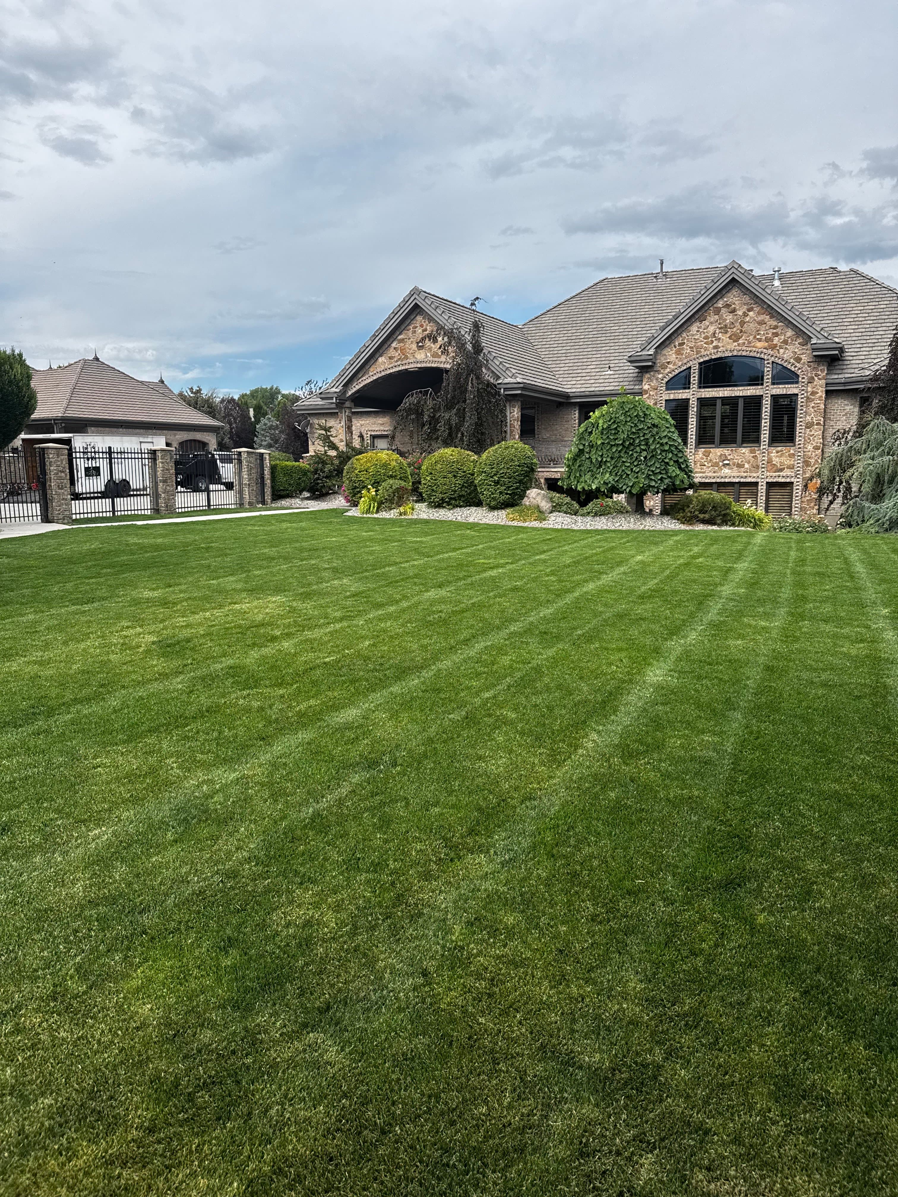 Striped lawn maintained by Everwork in front of a stone home