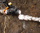 Repaired PVC sprinkler line and valve exposed in a dug-out trench